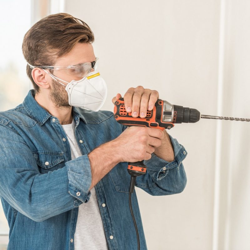 young-man-in-protective-mask-and-goggles-using-electric-drill-during-house-repair.jpg